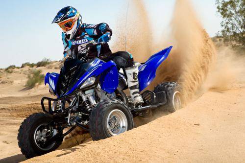 First Service: ATV (under 100cc) 6 A person rides a blue ATV over sandy terrain, wearing protective gear and a helmet. Dust trails behind as they maneuver through the desert landscape.