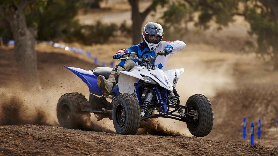First Service: ATV (under 100cc) 2 A person in protective gear rides a four-wheeler ATV on a dirt track, creating a trail of dust.