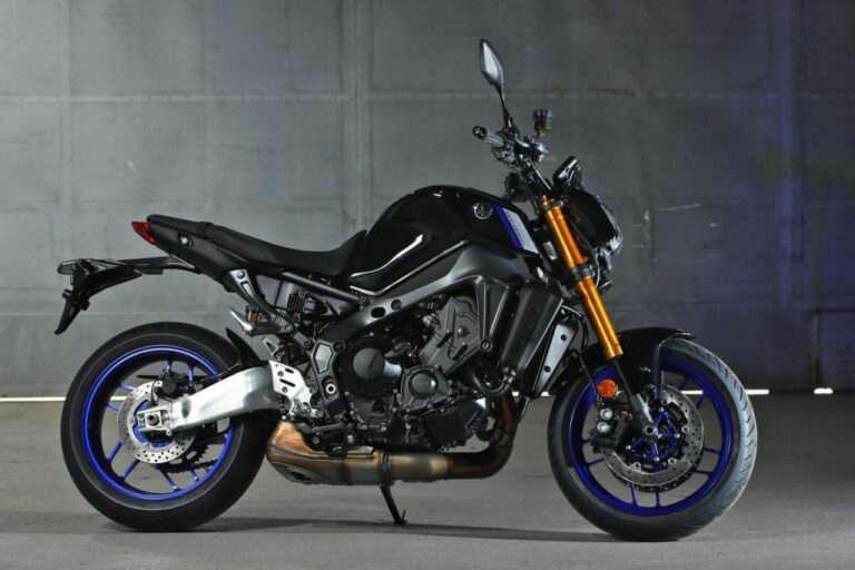 A sleek black Yamaha MT 09 with striking blue accents is parked elegantly on a concrete floor, positioned against a gray wall backdrop.
