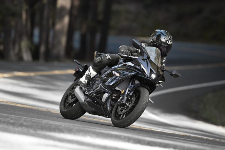 A person in full riding gear leans into a curve on a sleek, black motorcycle on a paved, winding road.