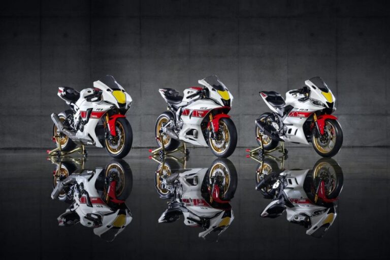 Three sport motorcycles with white, red, and black designs are displayed on stands against a gray concrete wall, with their reflections visible on a glossy surface.